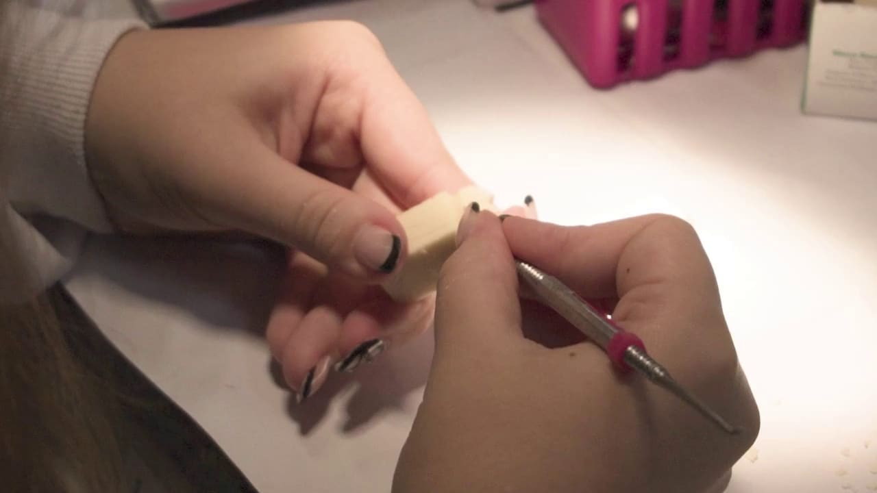Mãos esculpindo um dente em cera com um instrumento fino