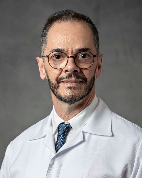 Prof. Sérgio Gonçalves de jaleco, sorrindo, em retrato de estúdio